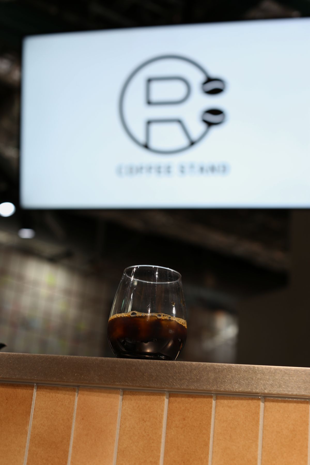 カウンターに置かれたグラスのコーヒーと、奥に光るロゴのサイネージ
