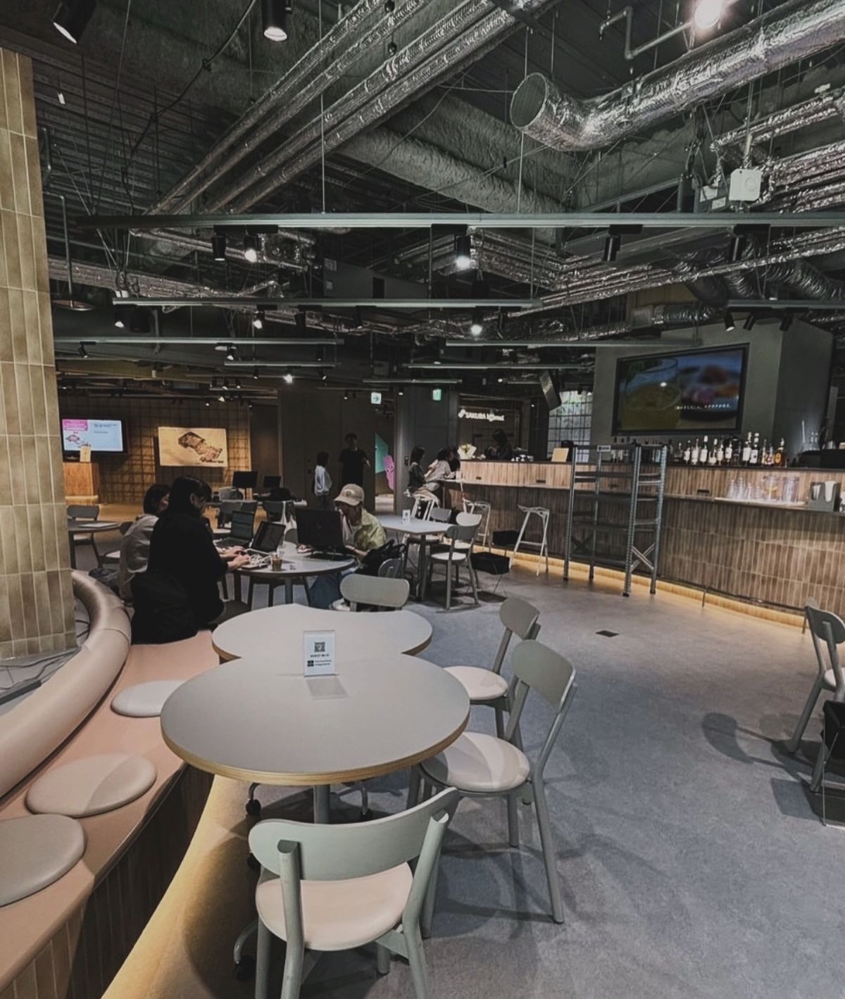 会場の Blooming kitchen。天井の配管がむき出しの広いフロアに、テーブルと椅子が並ぶ